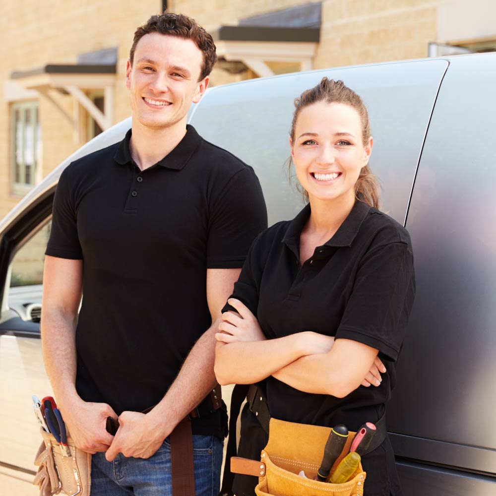 A man and woman are stood in front of a van with tool belts around their waist