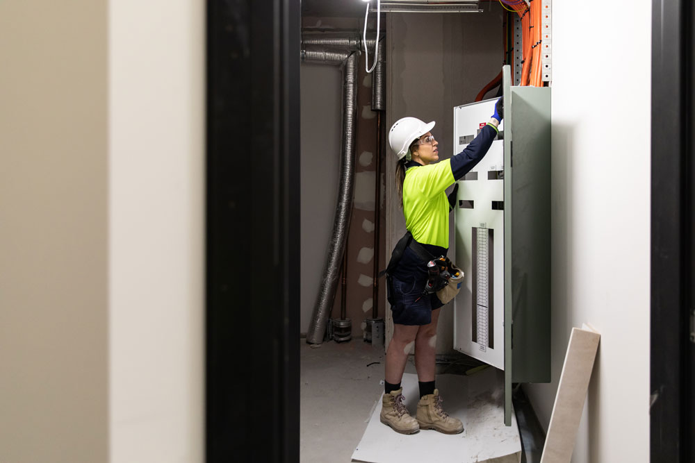 A person wearing protective head gear and a utility belt is performing a maintenance task.