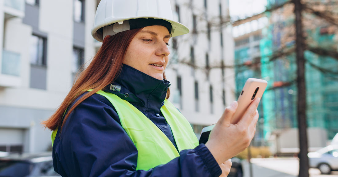Woman in hard hat and reflective vest looking at scheduling software on her phone