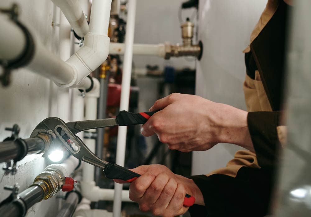 Two hands holding a wrench attached to pipework