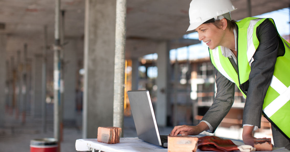 Person at construction site in yellow reflective vest and hard had looking at a computer