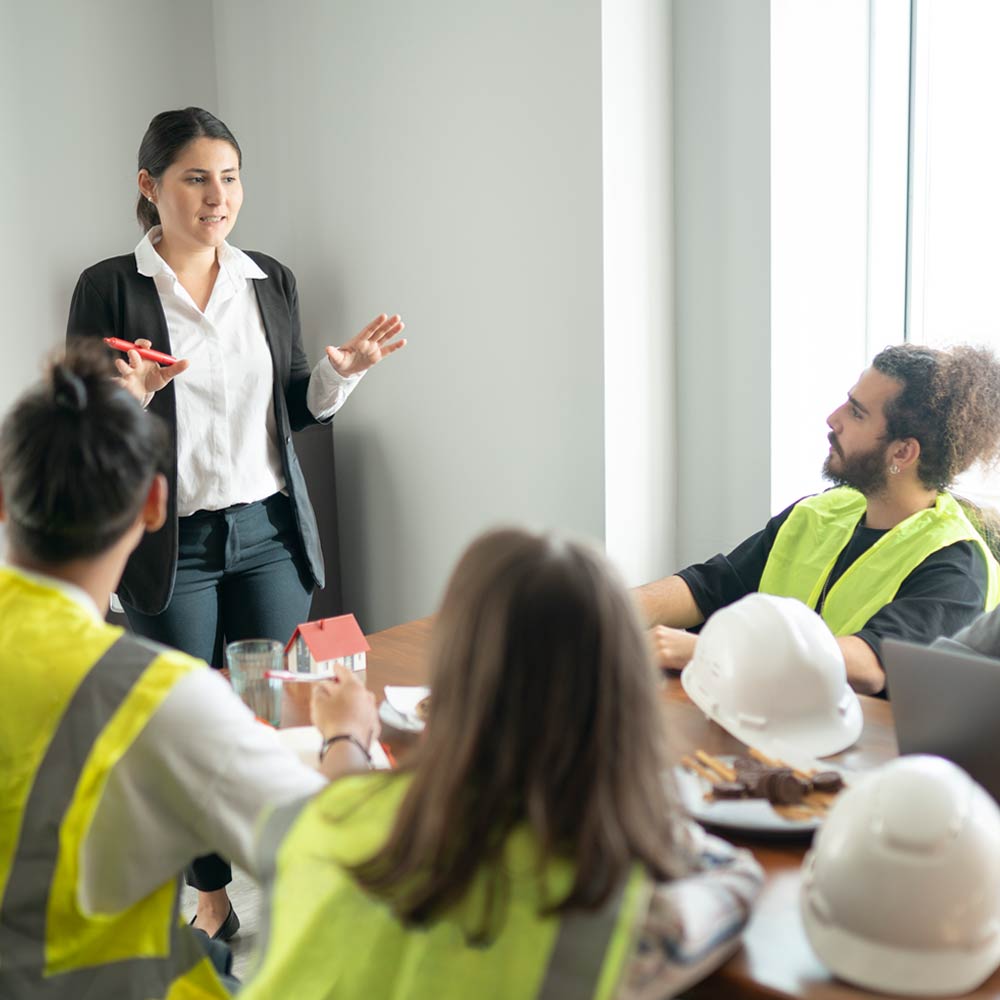 A person is stood up talking to a group of people who are wearing high visibility vests