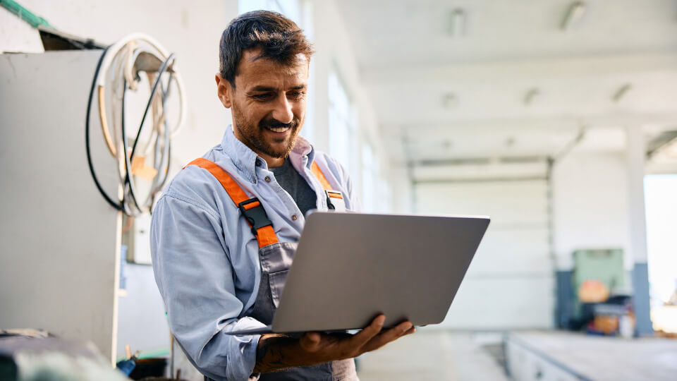 A man stands working on his laptop with a workshop around him