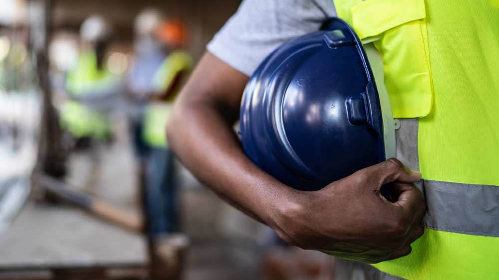 Contractor in reflective vest holding hardhat under their arm