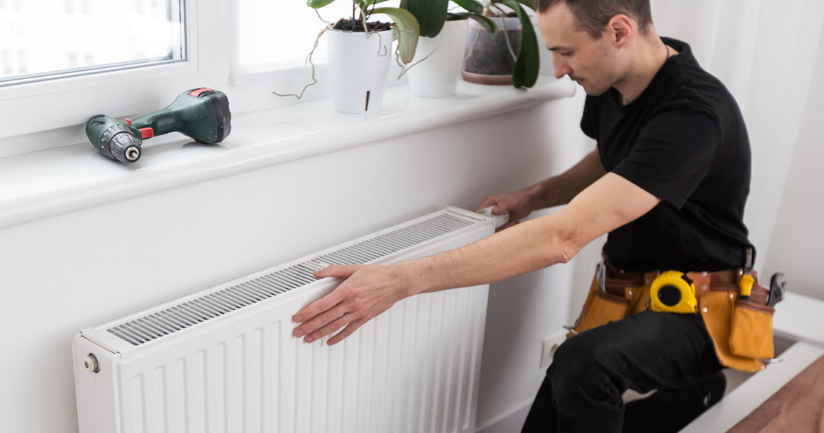 A person wearing all black and a toolbelt is performing maintenance on a radiator