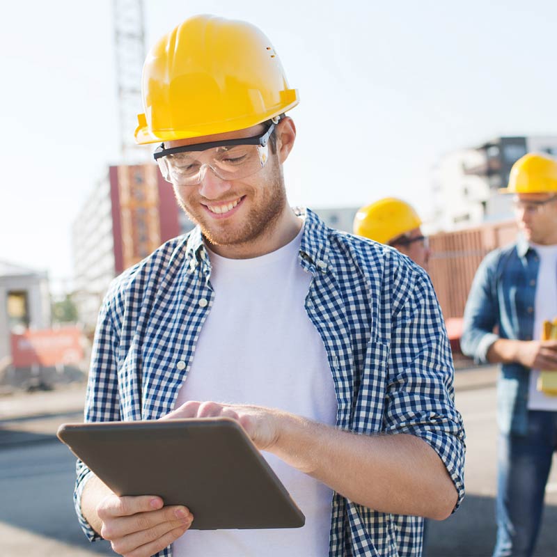 Man looking at tablet device wearing goggles and a yellow hard hat