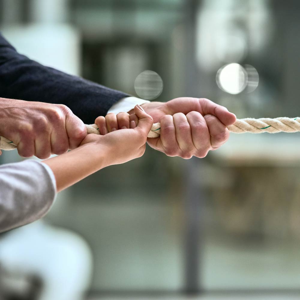 Three hands can be see holding a large rope as if pulling in a tug of war