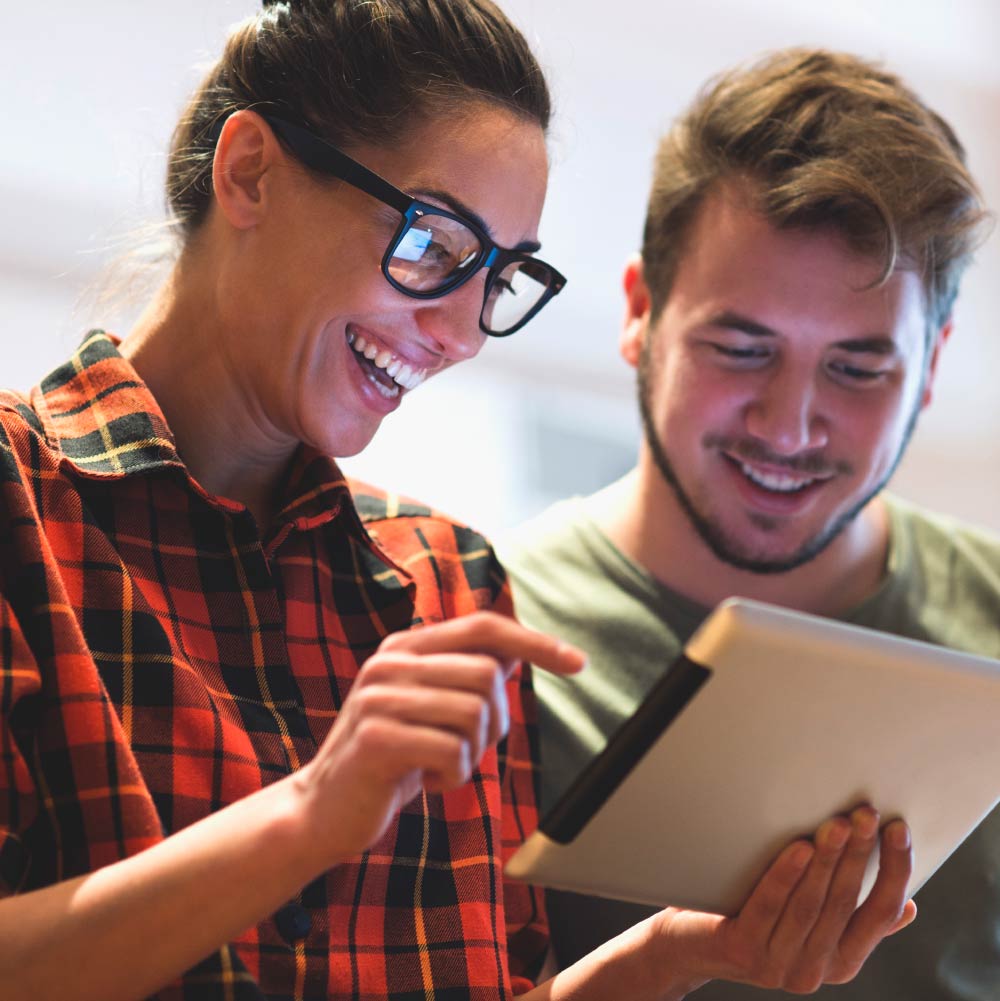 Two people are laughing and smiling while looking at a tablet device