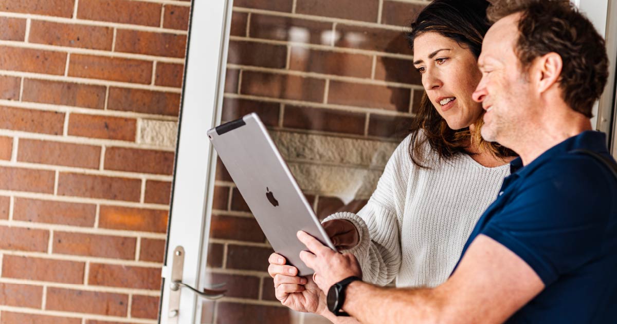 Two people are stood in a doorway looking at a tablet device and smiling