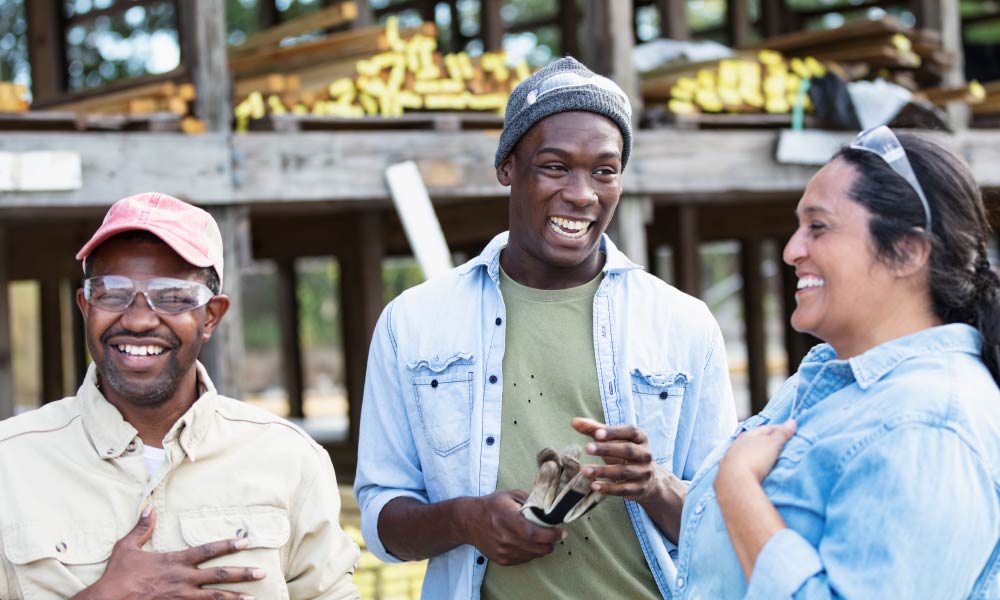 Three people are stood together smiling and laughing