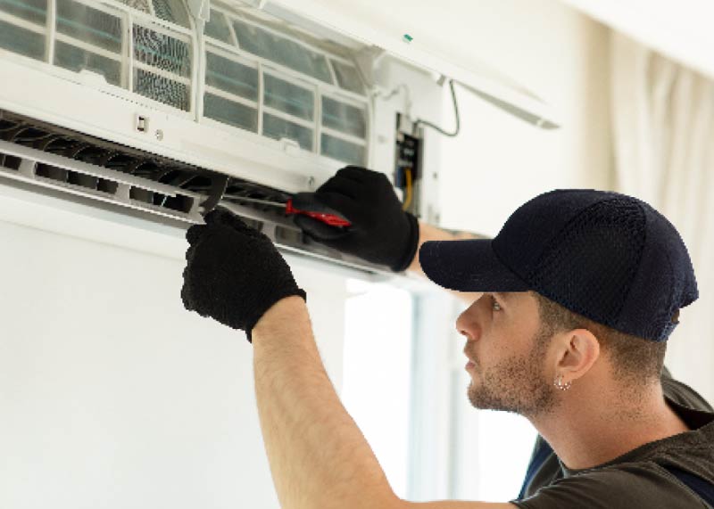 Man holding screwdriver maintaining air conditioning unit