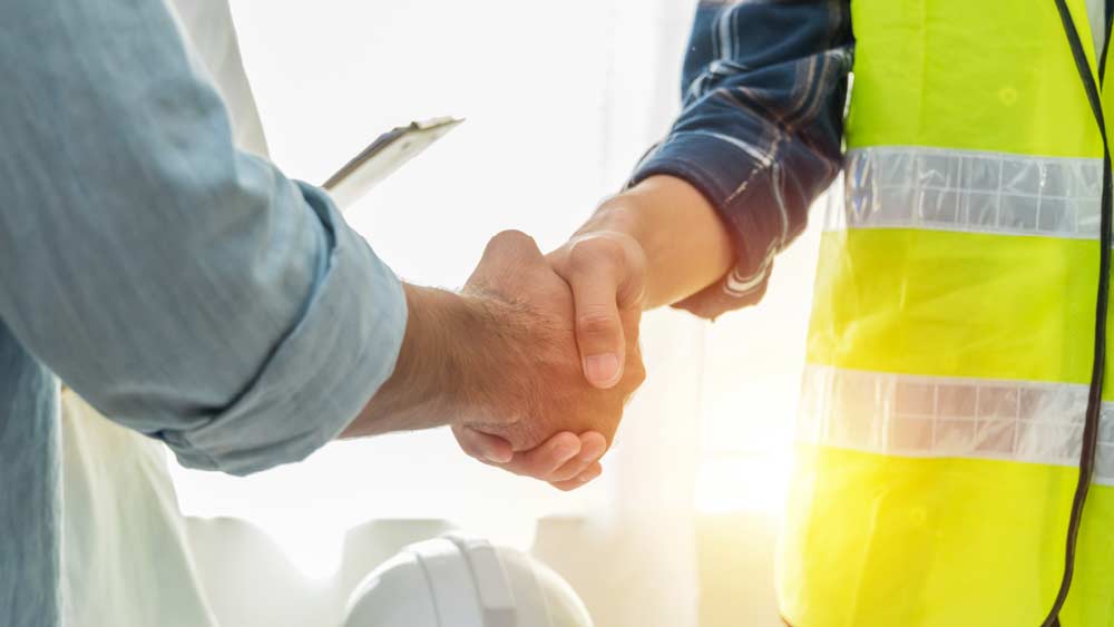 Two people shaking hands and one person is wearing a high visibility vest