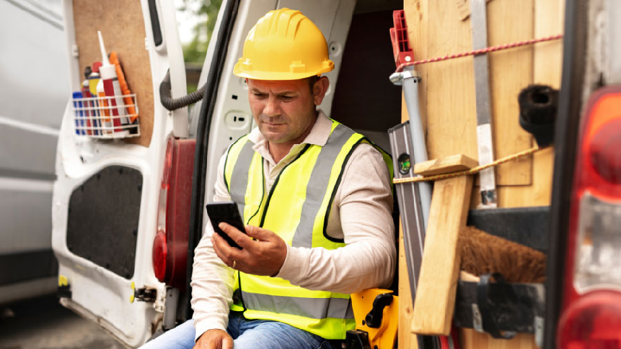 A tradesman sitting in a work van, looking at a mobile device.