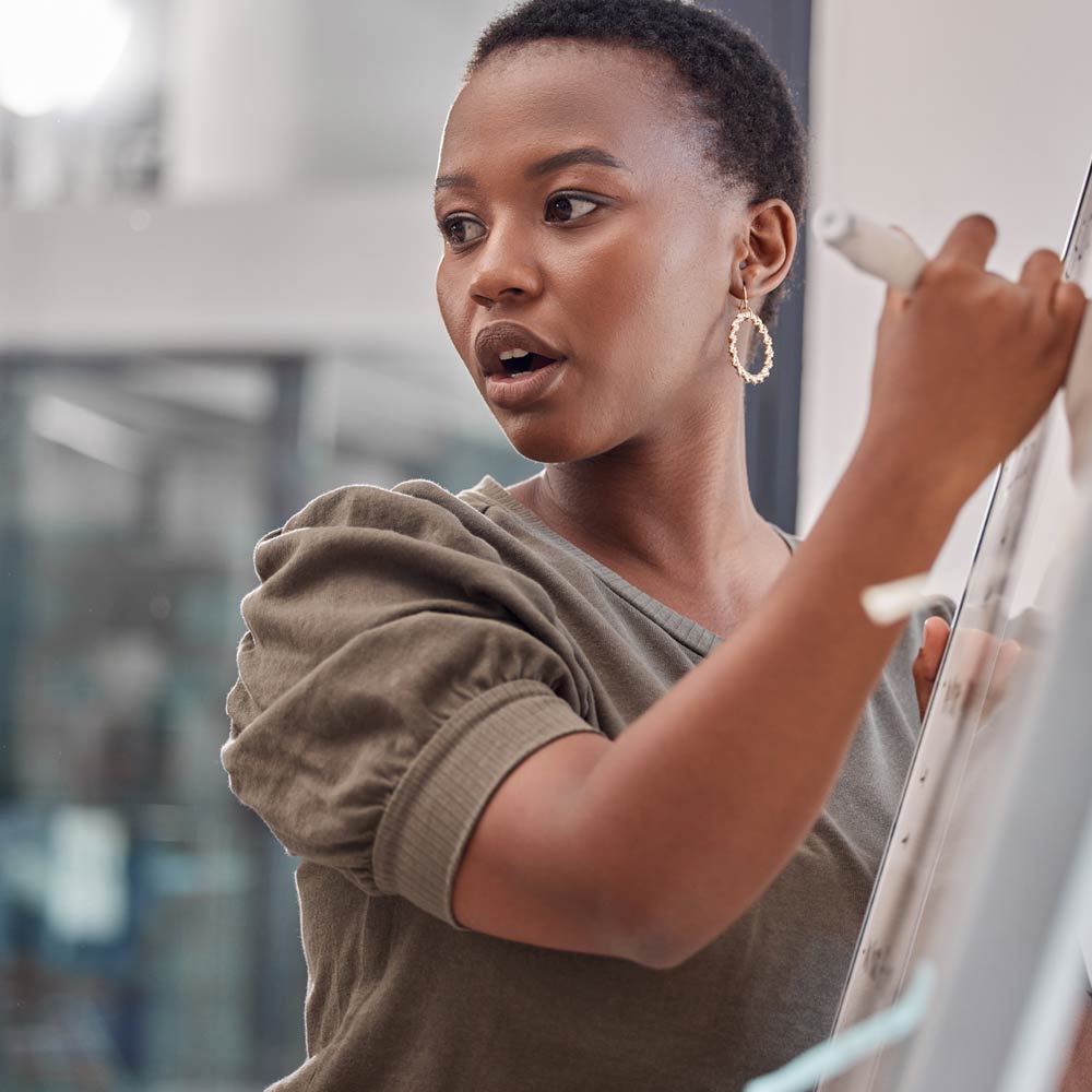 A person is stood to the side of a whiteboard holding a whiteboard pen about to write