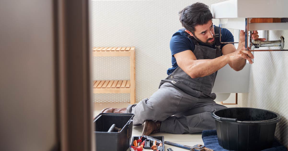 Male plumber working with tools under a sink