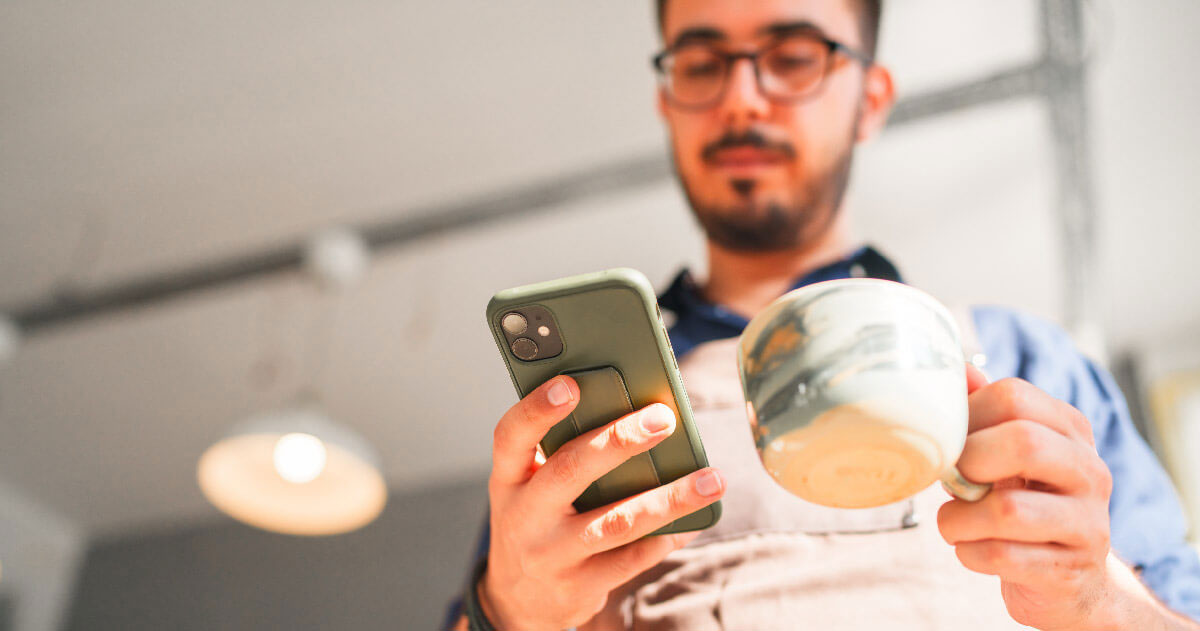 A person is holding a smartphone in one hand and a mug in the other, staring down towards the smartphone.