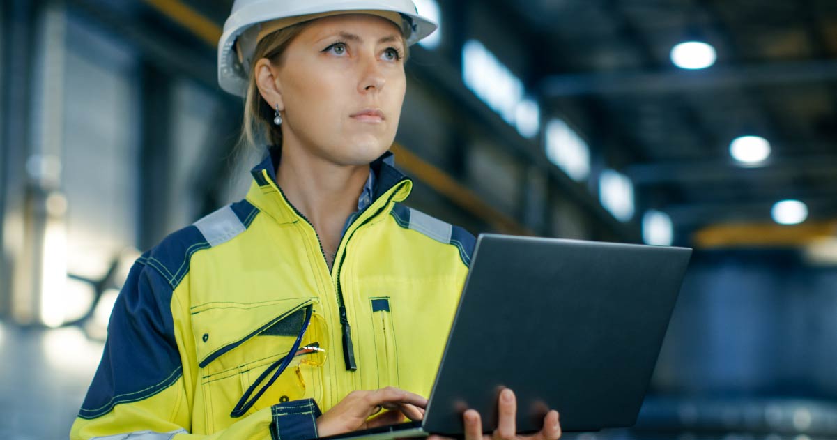Woman wearing protective gear, holding open laptop looking out into the distance confidently