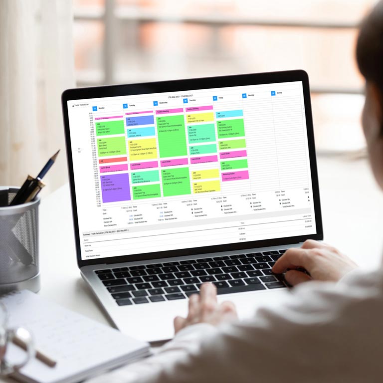 A Simpro timesheet displaying on a laptop screen with hands hovering above the keyboard