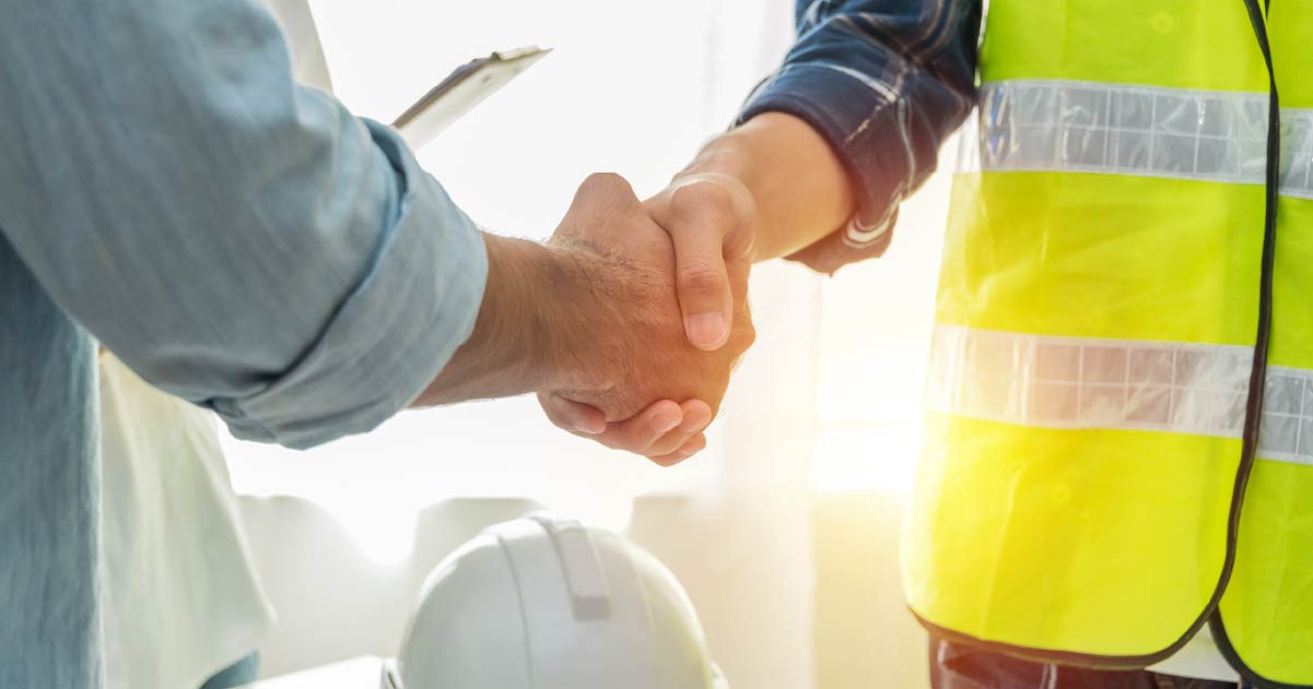 Two people shaking hands with one wearing a yellow high visibility jacket and the other in a blue shirt.