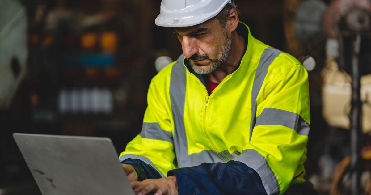 Man in hard hat and reflective vest working on computer to implement field service management best practices