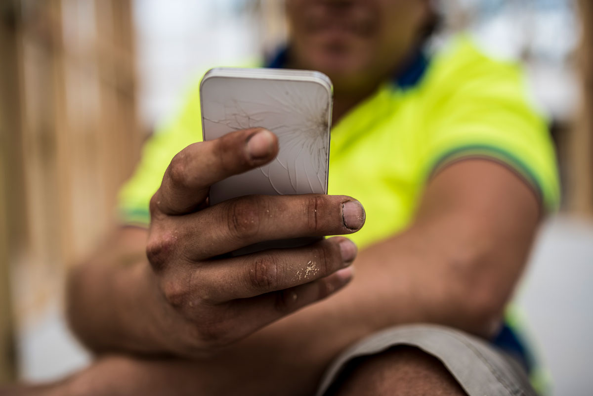 Close up of hand holding broken phone with person in yellow shirt in background