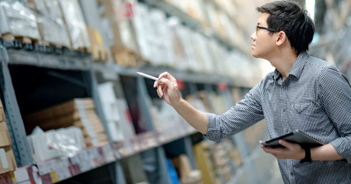 A person is stood in a warehouse holding a tablet device and pointing in the air with a stylus