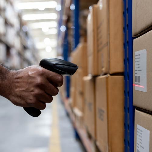 A hand is holding a barcode scanner pointed towards a cardboard box