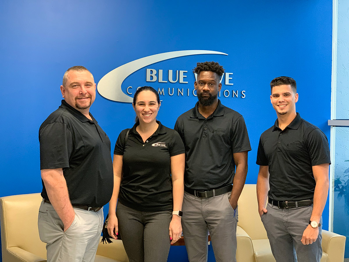 Blue Wave Communications staff members in front of company logo