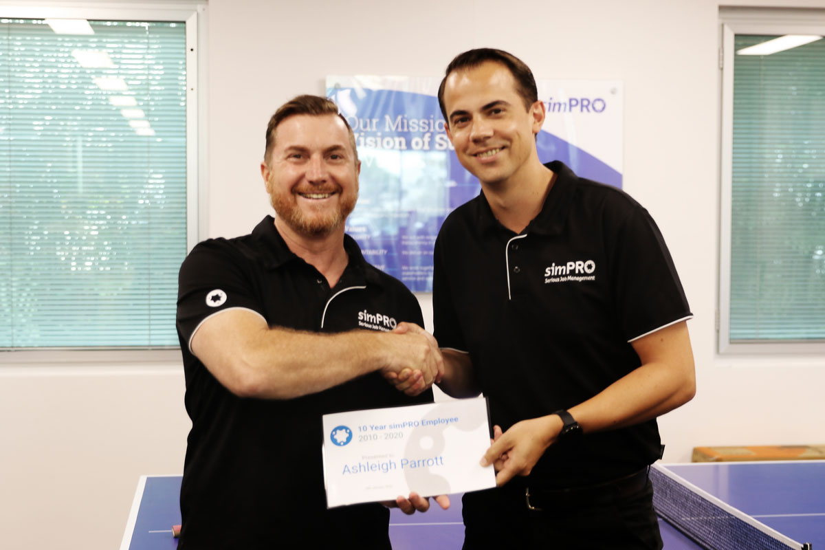 Business Development Manager Ash Parrott holding a certificate and shaking hands with Simpro employee