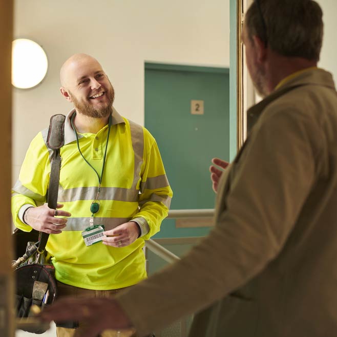 A person stood in the doorway with a identification badge around his neck and smiling towards another person in the doorway but out of focus.